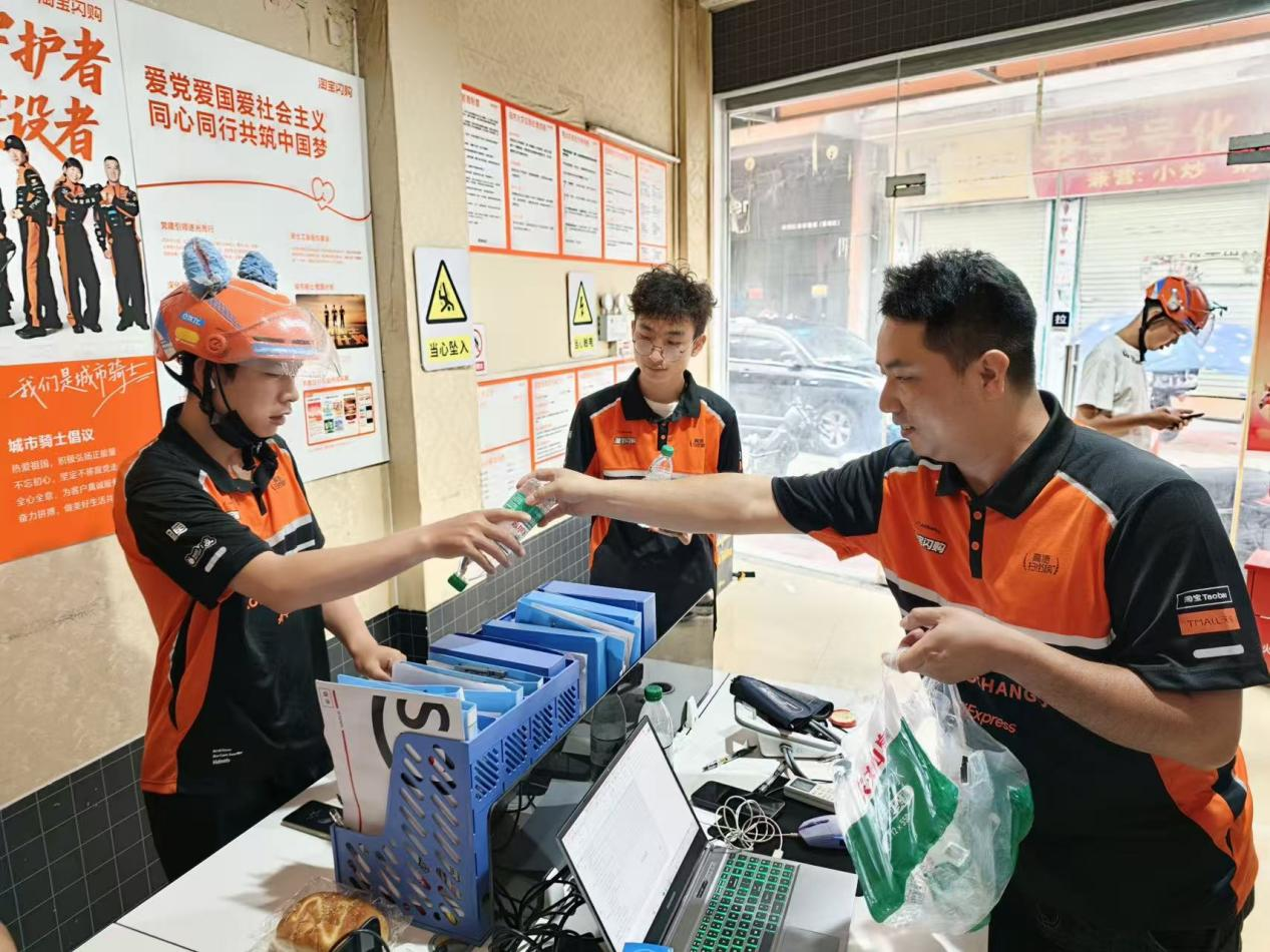 欧阳任兵（右）给站点骑手发放矿泉水。人民网记者 王雅蝶摄
